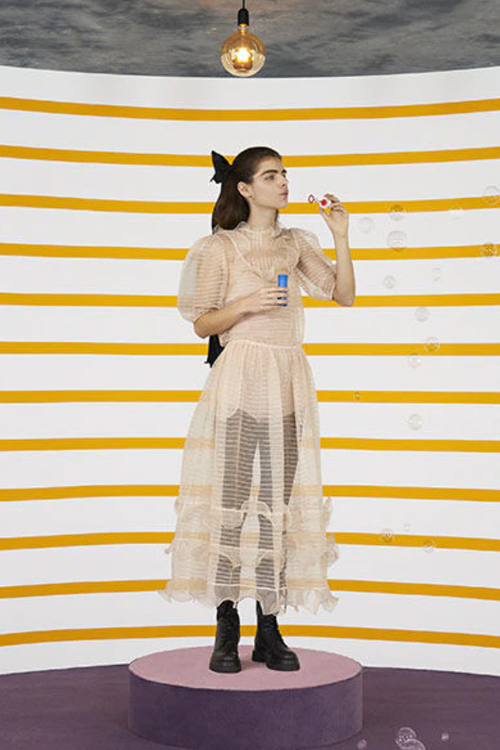 Tanara in rochie transparenta facand balaone de sapun, fundal alb cu dungi galbene